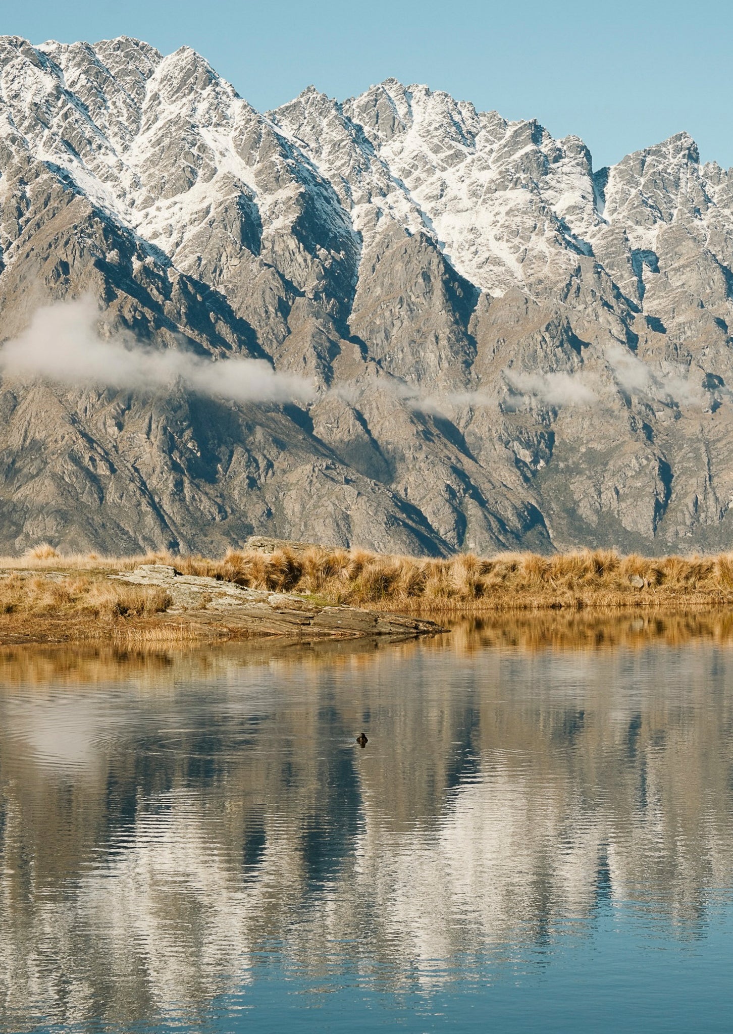 Mountain range reflected in a calm body of water with a clear blue sky.