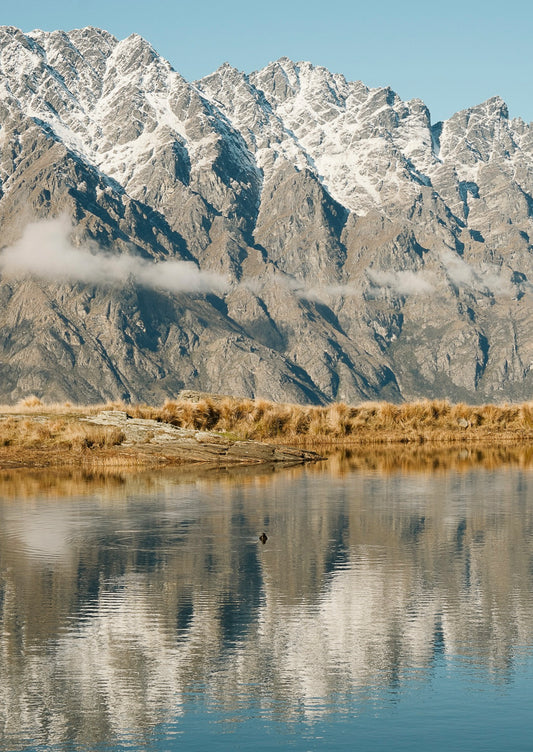 Mountain range reflected in a calm body of water with a clear blue sky.