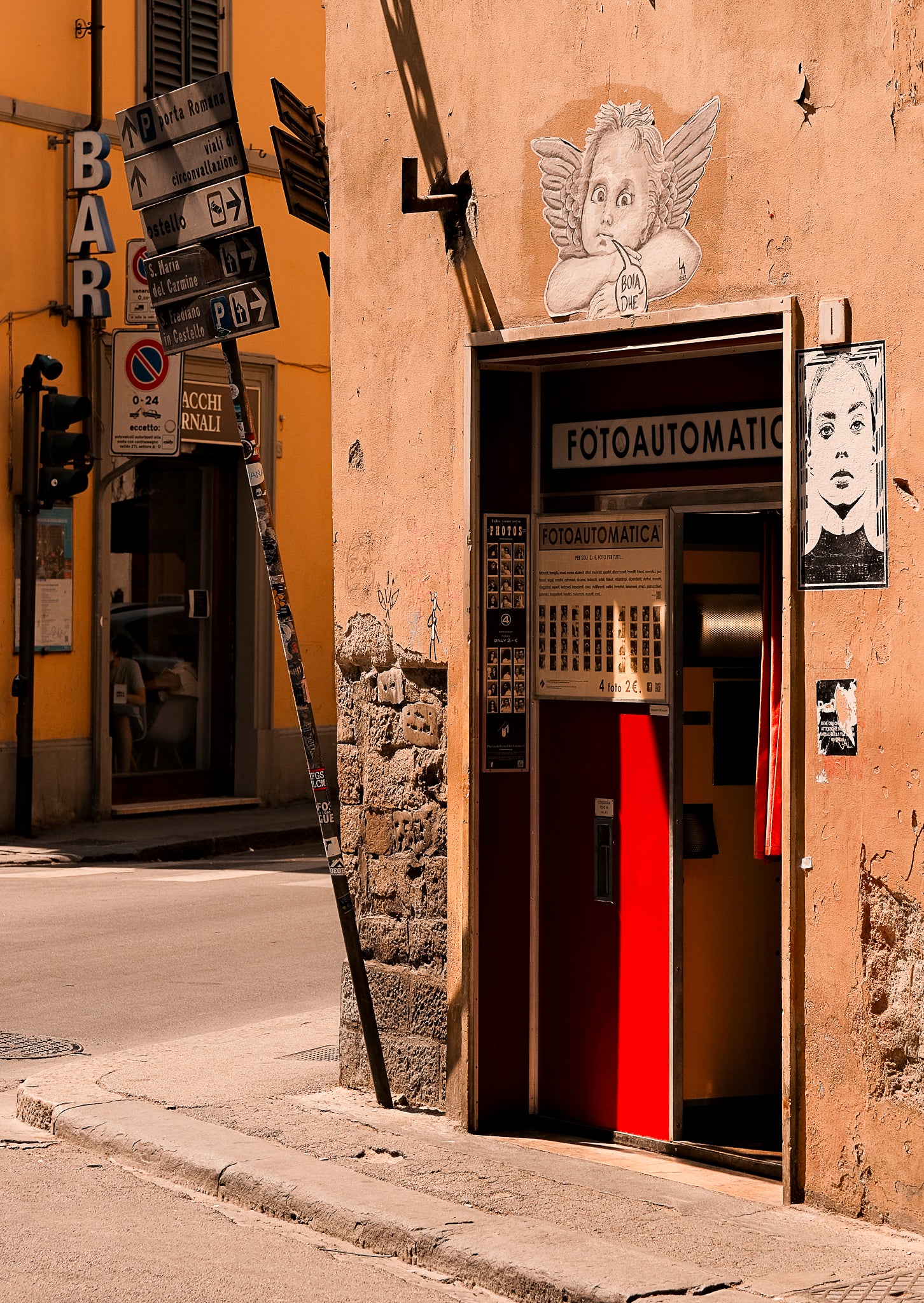 Vintage photo booth on a street corner with street signs and a yellow building in the background.