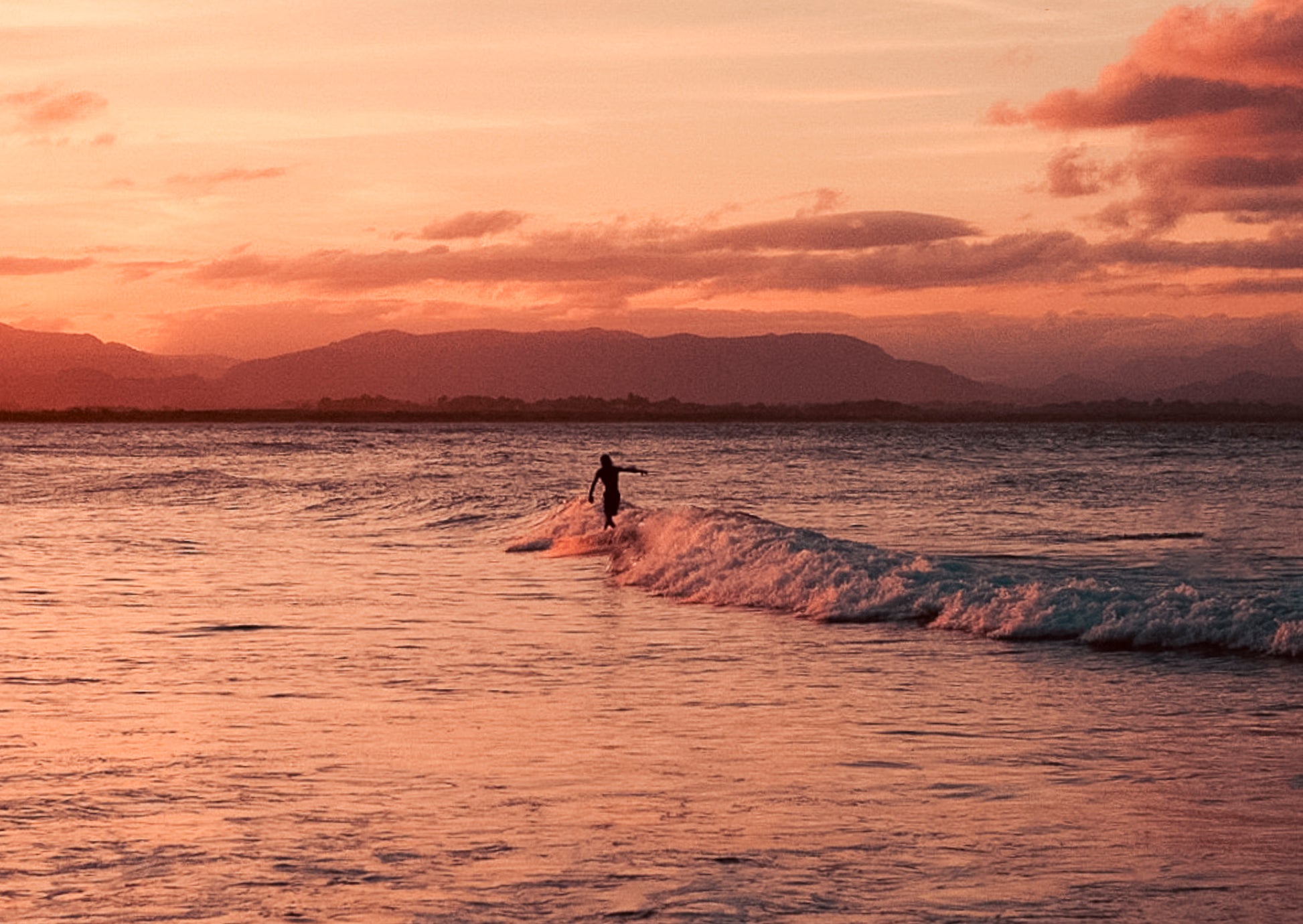 Person surfing at sunset with mountains in the background