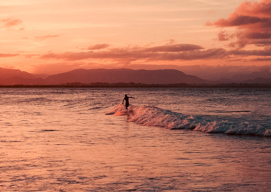 Person surfing at sunset with mountains in the background