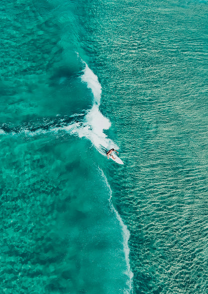 Surfer riding a wave in clear blue water from an aerial perspective