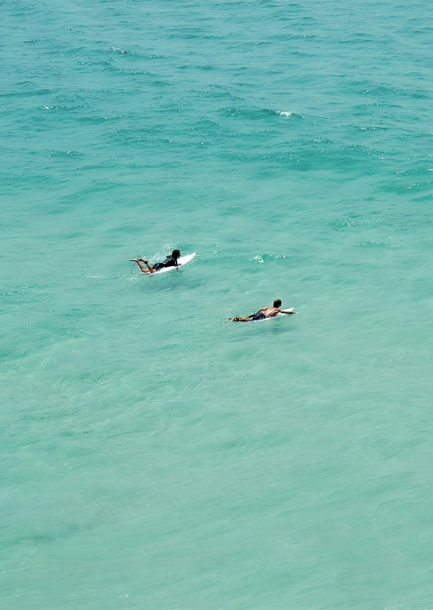 Two people surfing in clear blue water