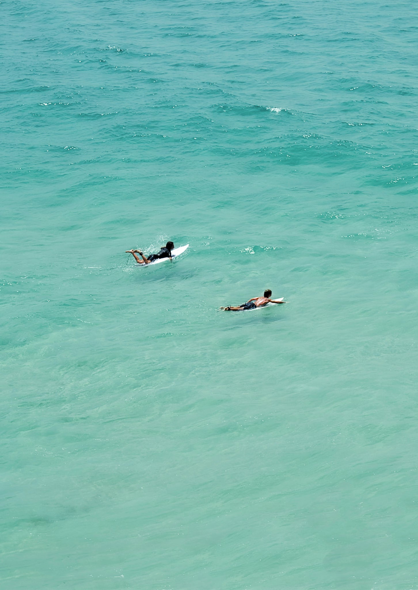 Two people surfing in clear blue water